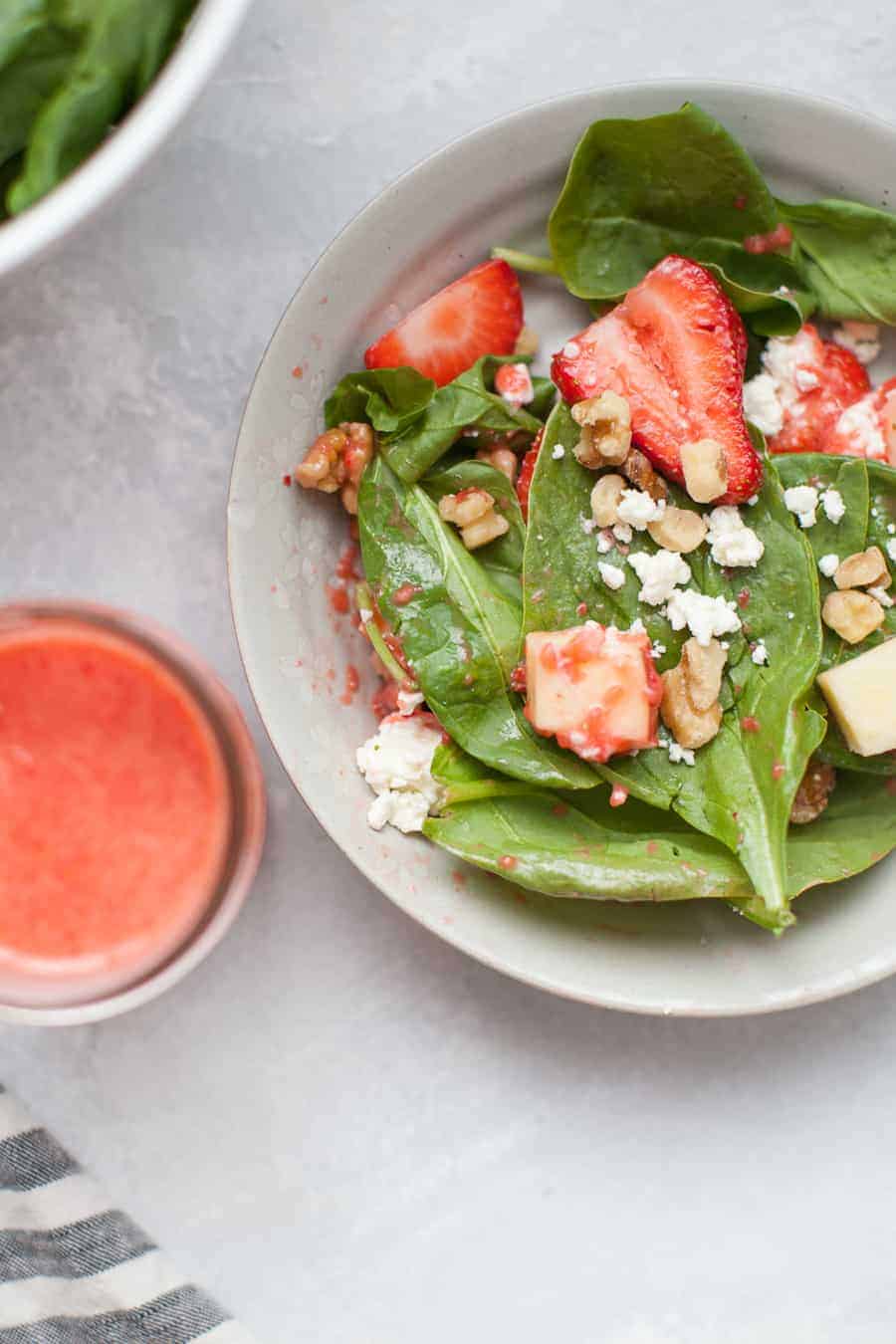 A bowl of strawberry spinach salad with a mason jar of strawberry vinaigrette sitting next to it.