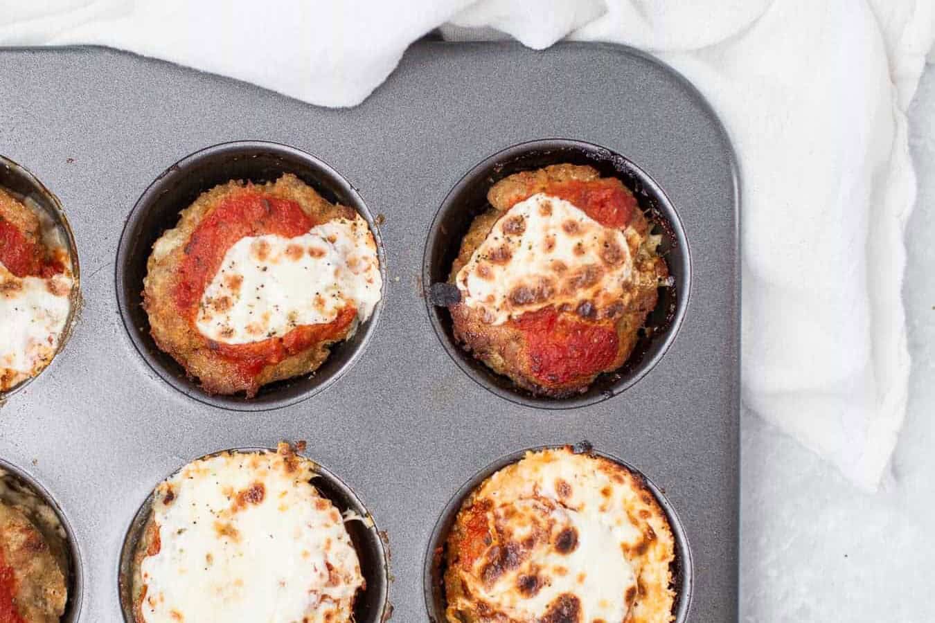 Baked mini meatloaves topped with tomato sauce and cheese in a muffin tray.