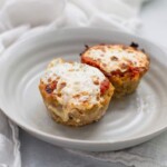 Two baked turkey meatloaf muffins topped with melted cheese rest enticingly on a pristine white plate.
