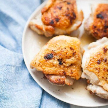 Plate with four pieces of crispy, lemon pepper chicken thighs. A light blue cloth is placed nearby.