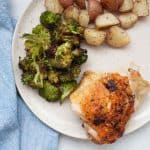 Close up of crispy chicken thigh with lemon pepper seasoning plated with broccoli and potatoes.