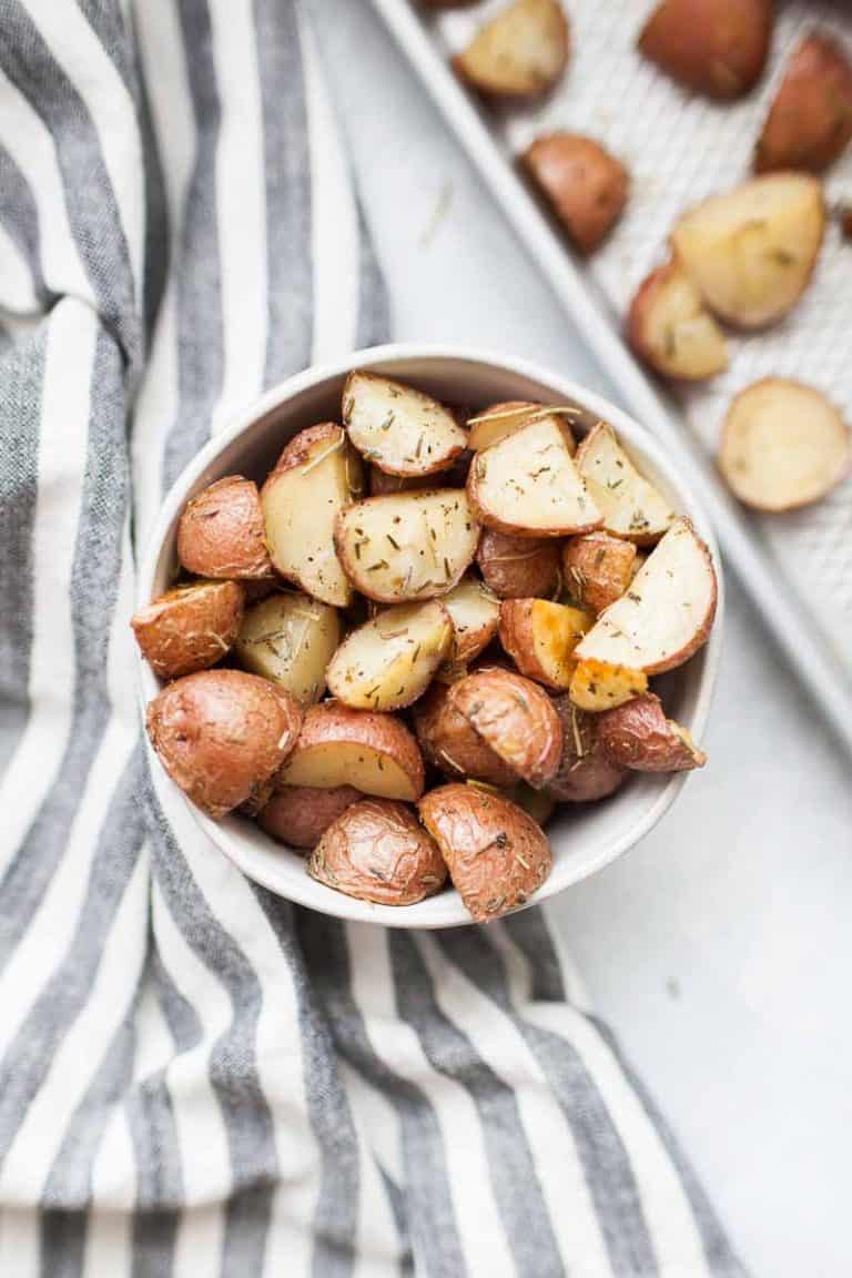 A bowl of rosemary roasted red potatoes next to a sheet pan.