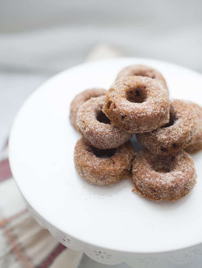 Stack of mini pumpkin donuts on a white cake stand.