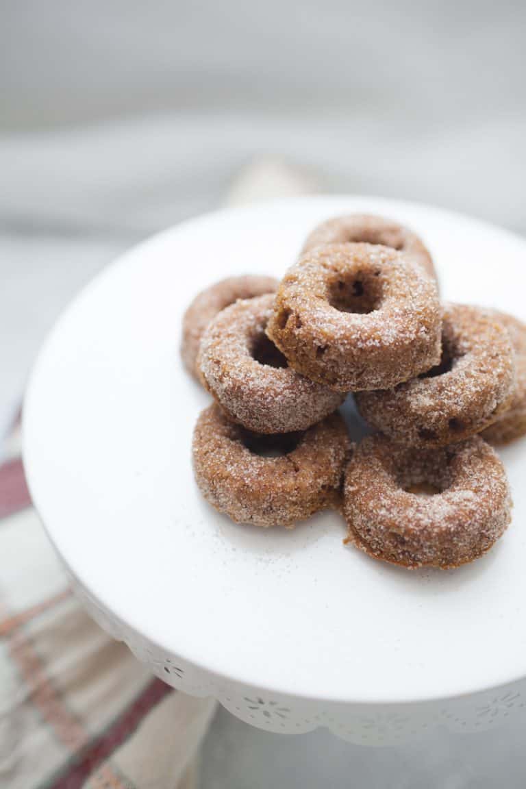 Stack of mini pumpkin donuts on a white cake stand.