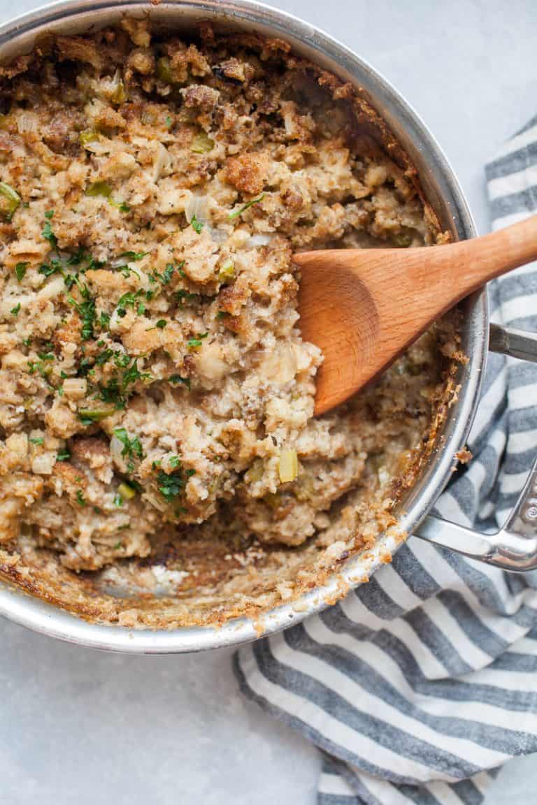 Stainless steel skillet filled with cooked stovetop sausage stuffing with a wooden spoon sticking out of the pan.