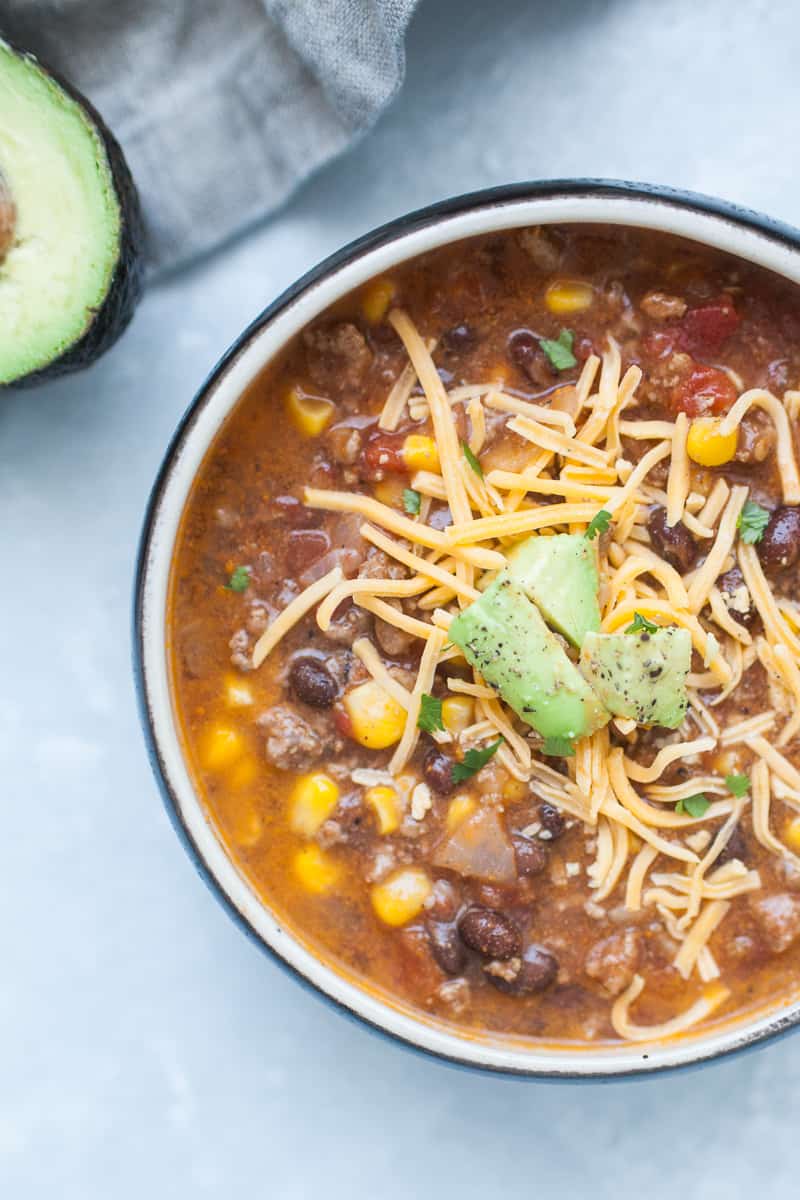 Black soup bowl with taco soup, ground beef, corn, beans, tomatoes, cheese and avocado.