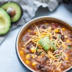 Black soup bowl with taco soup, ground beef, corn, beans, tomatoes, cheese and avocado.