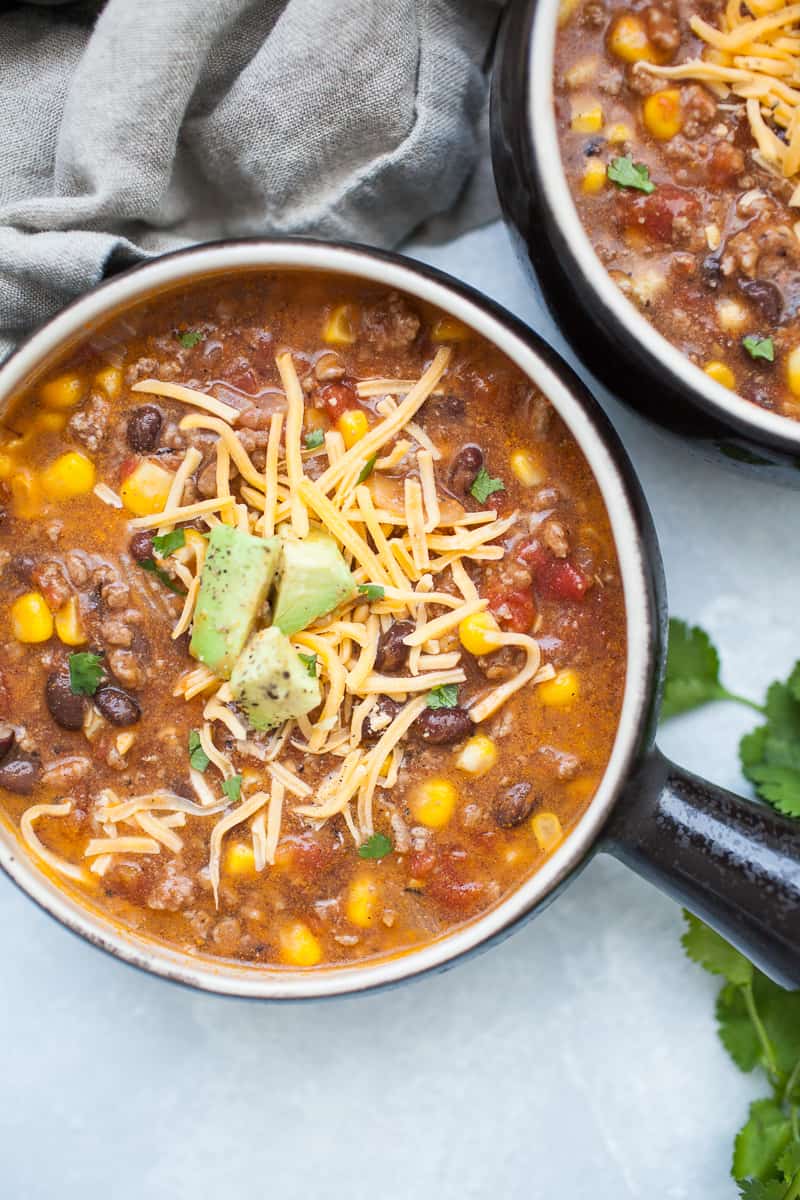 Black soup bowl with taco soup, ground beef, corn, beans, tomatoes, cheese and avocado.