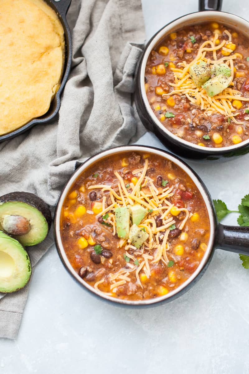 Black soup bowl with taco soup, ground beef, corn, beans, tomatoes, cheese and avocado.