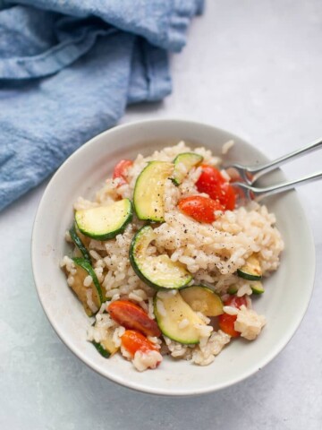 Gray bowl with vegetable risotto on top of a blue linen napkin.