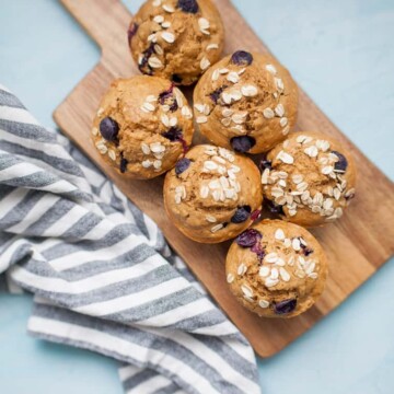 Freshly baked blueberry oatmeal muffins on a wooden cutting board.