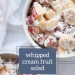 Close-up of a bowl filled with whipped cream fruit salad, containing grapes, bananas, and other mixed fruits, with a text overlay that reads "whipped cream fruit salad." Another similar bowl is partially visible next to a tray of ginger molasses snickerdoodles.