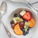 a small bowl of fruit salad with a silver spoon on a white and blue stripe kitchen towel