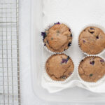 muffins in a tupperware on paper towels next to a cooling rack