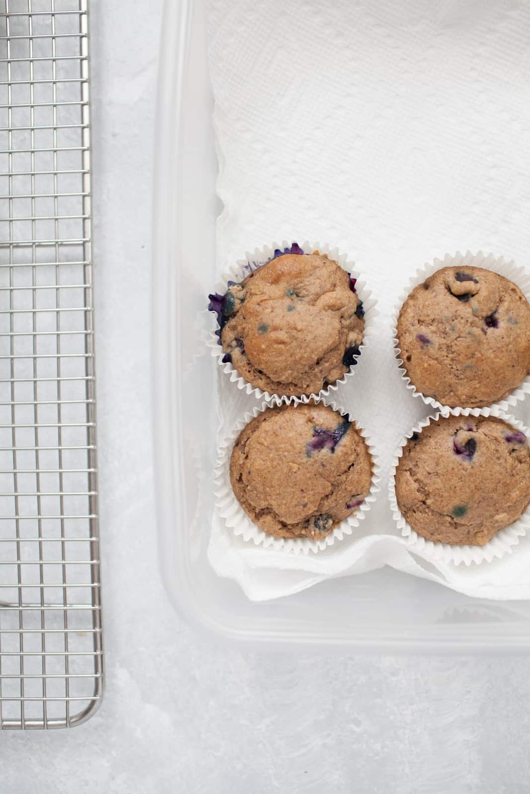 muffins in a tupperware on paper towels next to a cooling rack