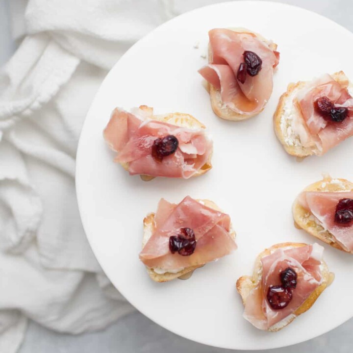 top view of Cranberry Prosciutto Crostini with Goat Cheese on a white cake stand