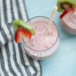 Strawberry kiwi smoothie in a glass with a slice of kiwi and strawberry slices on the rim of the glass.