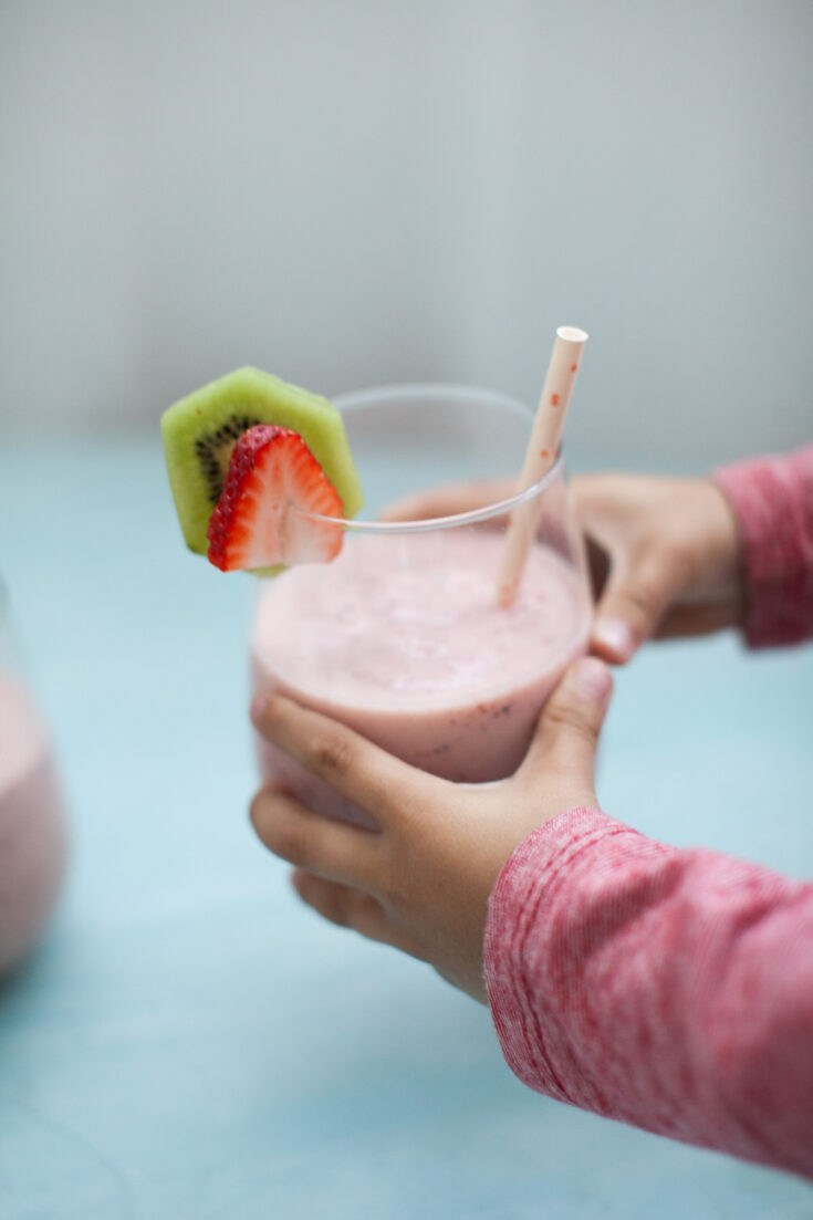 a boy's hands with red sleeves holding a strawberry kiwi smoothie