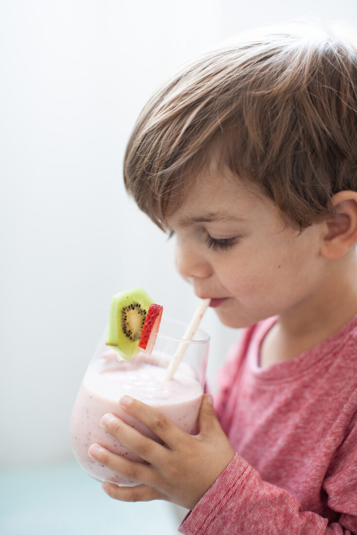 a blond boy sipping a strawberry kiwi smoothie