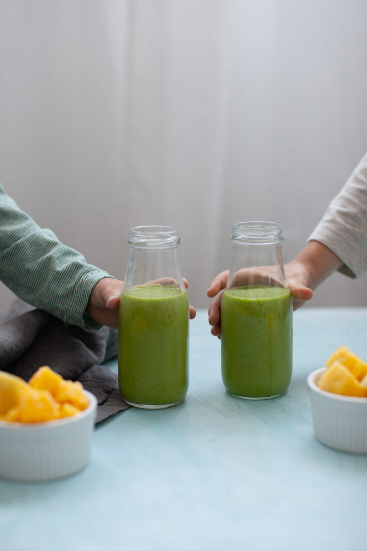 two kids' hands holding glasses of Green Smoothies