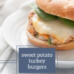 A close-up of a sweet potato turkey burger with melted cheese and spinach on a bun, placed on a white plate. The text overlay reads "sweet potato turkey burgers" with a website link "joyfullymad.com." Indulge in more flavors at Joyfully Mad, featuring lemon pepper chicken thighs and other delightful dishes.