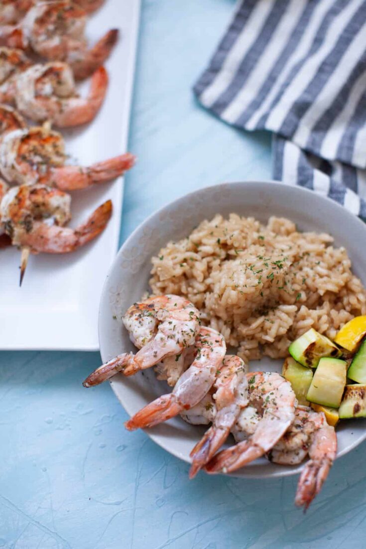 shrimp skewers on a plate next to a rice bowl