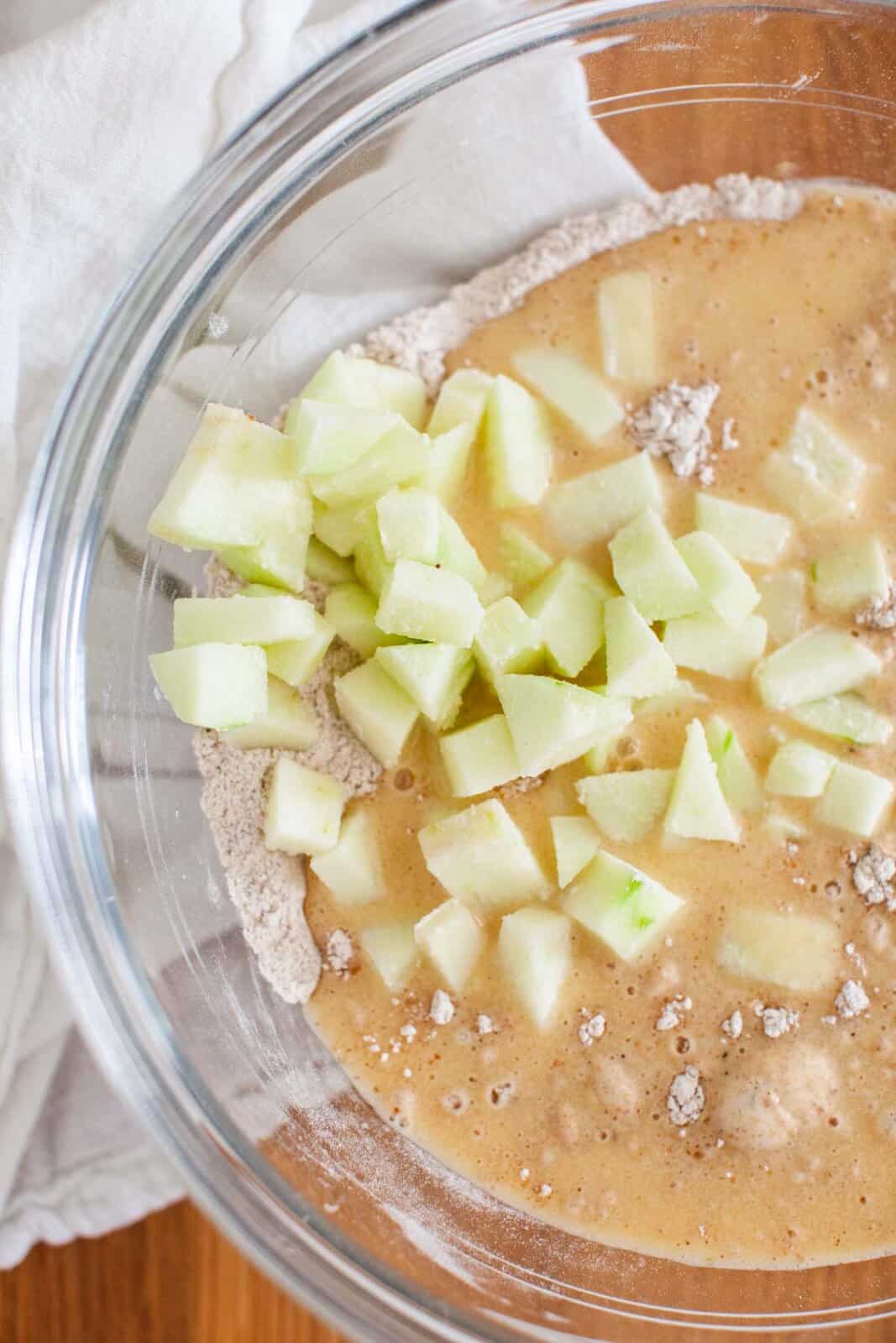 Diced green apples and batter in a clear mixing bowl.