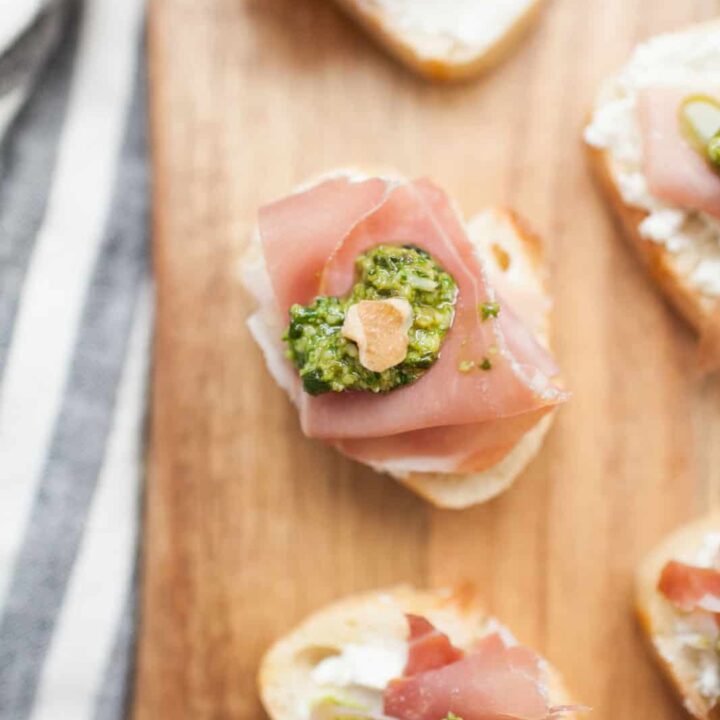 a pieced of bread with goat cheese, prosciutto, basil and walnuts