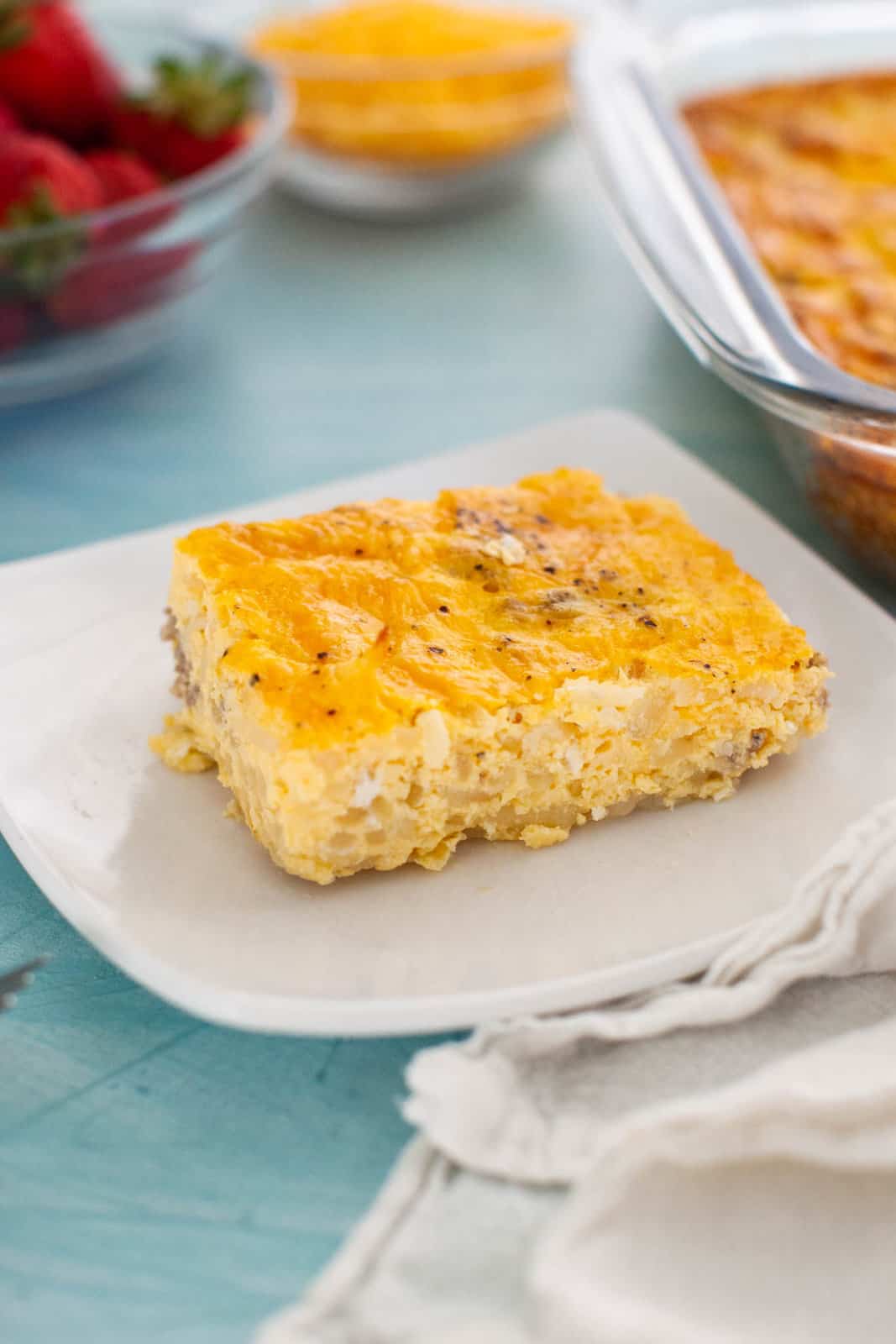 A plate with a slice of cheesy breakfast casserole on a blue table.