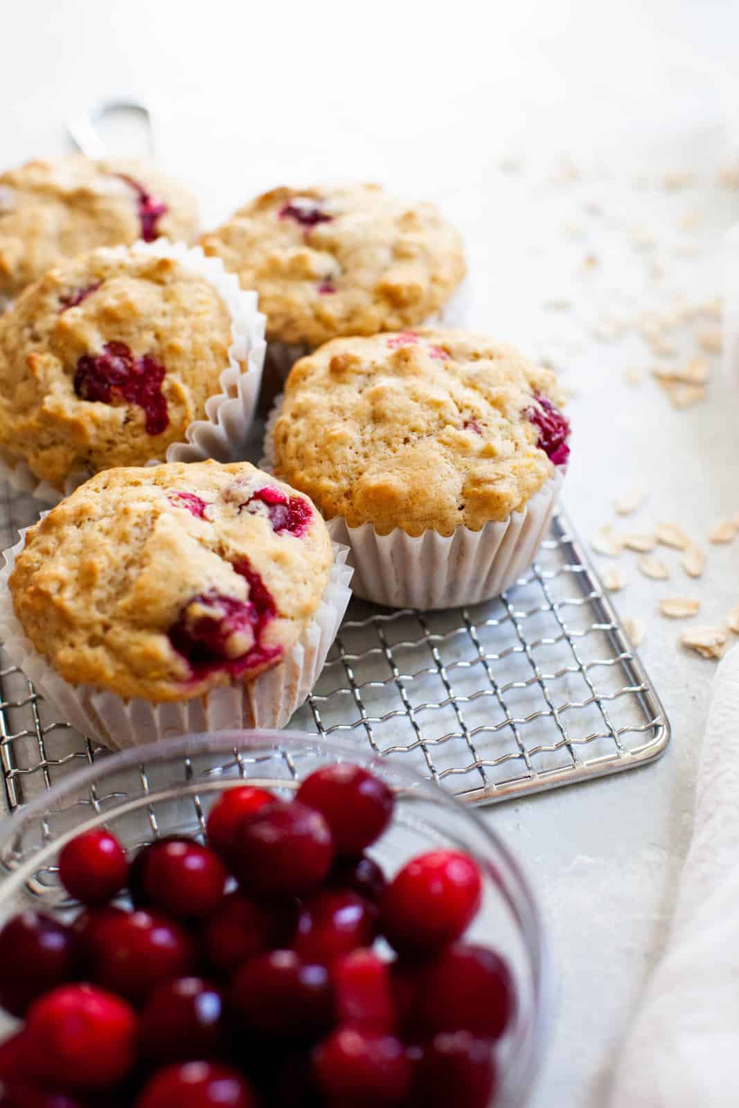 A bowl of fresh cranberries next to baked cranberry orange muffins.