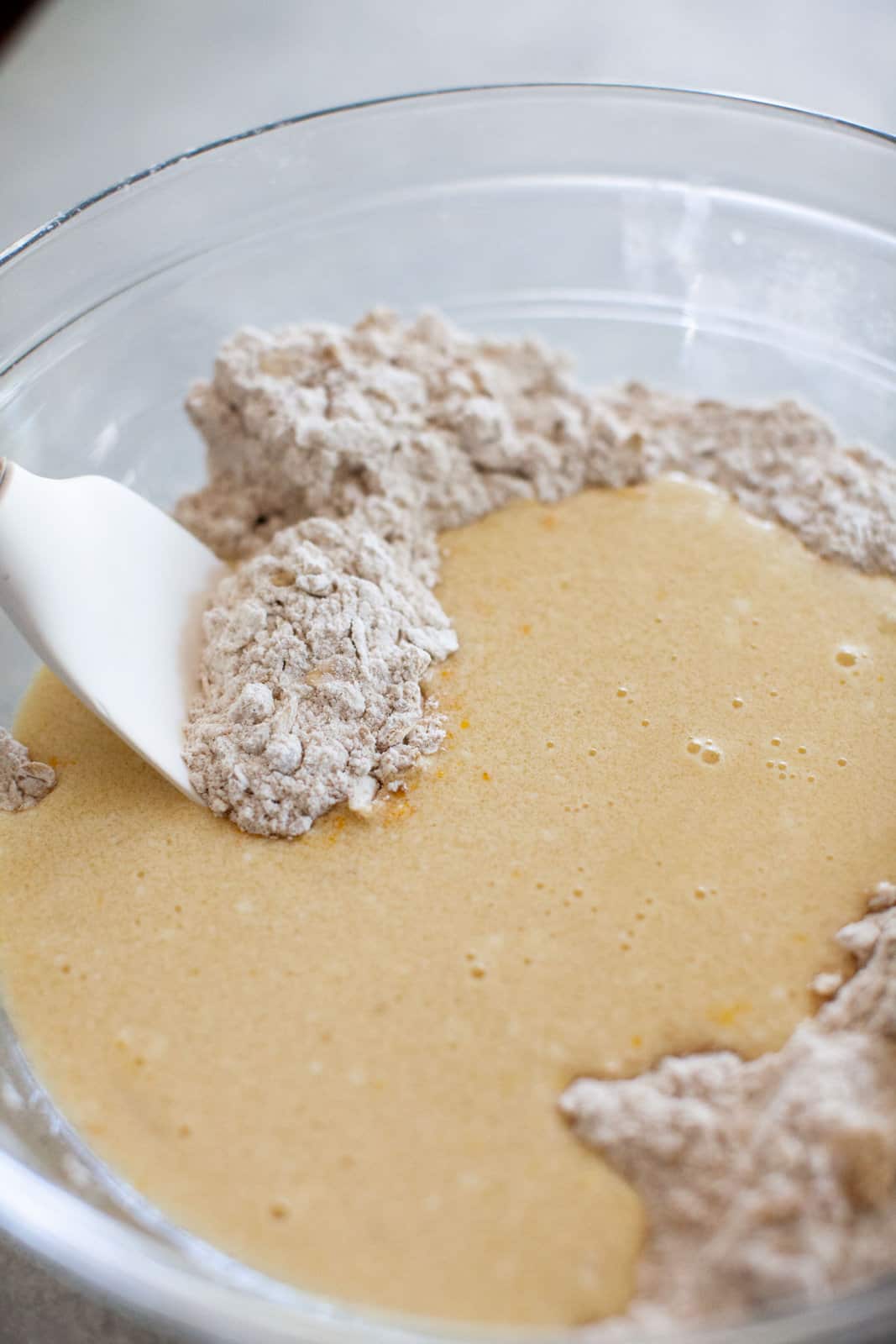 Mixing wet cranberry muffin ingredients into dry ingredients in a large glass bowl.