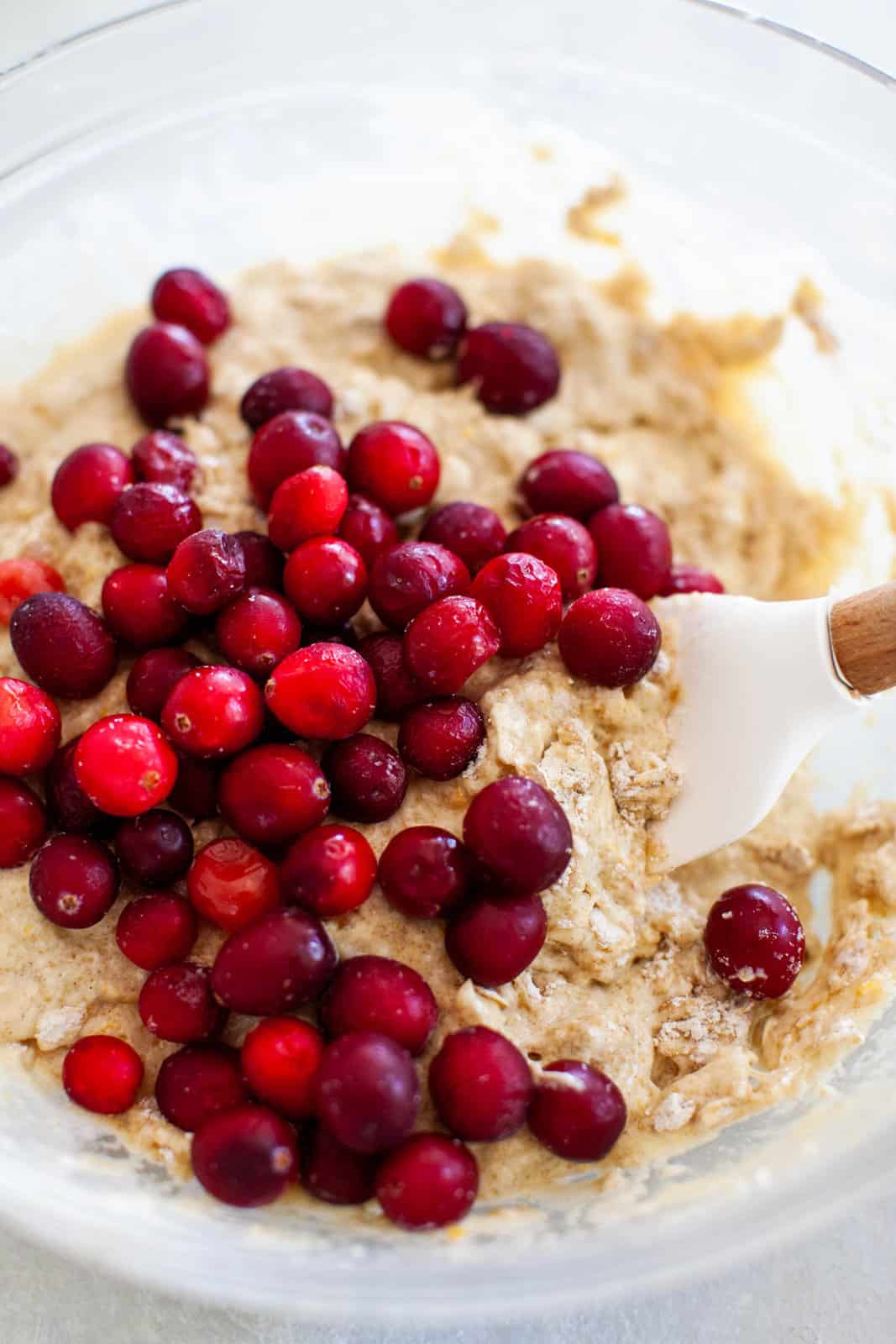 Folding frozen cranberries into muffin batter in a glass mixing bowl.