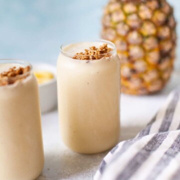 a glass of pineapple smoothie next to a kitchen towel and a fresh pineapple.