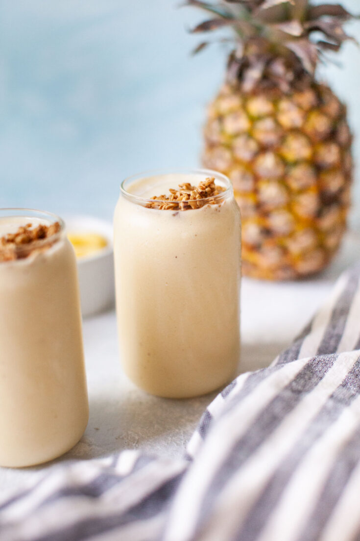 a glass of pineapple smoothie next to a kitchen towel and a fresh pineapple.