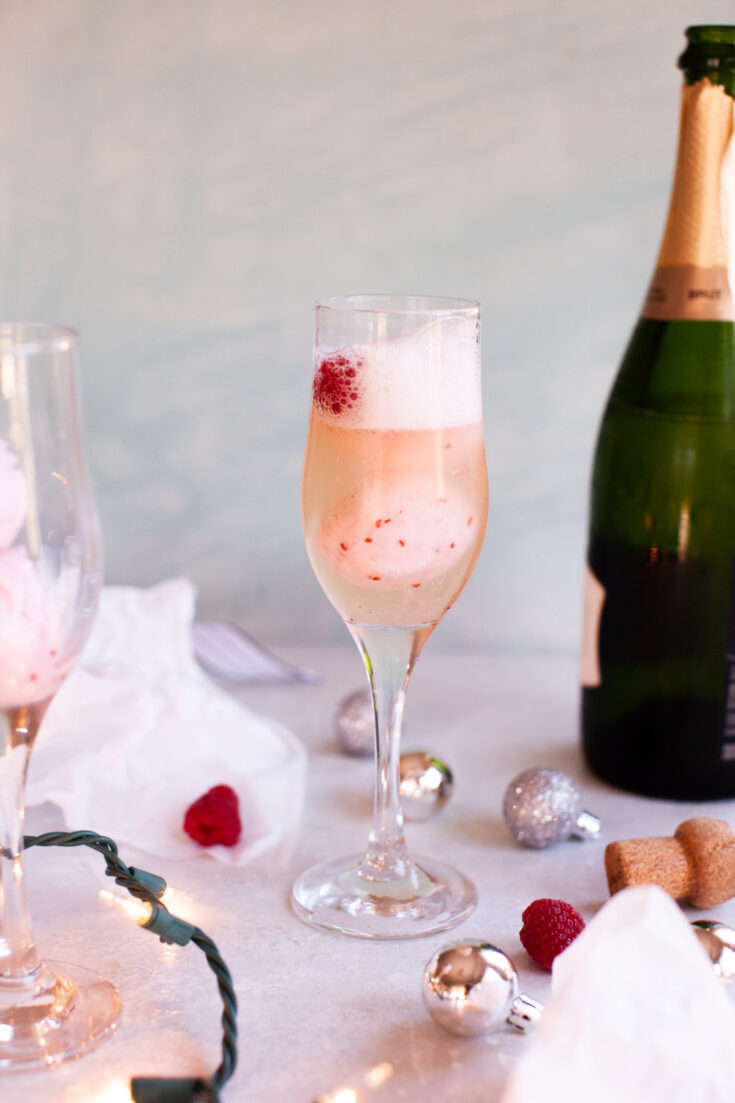 one raspberry float with champagne next to a bottle of sparkling wine.