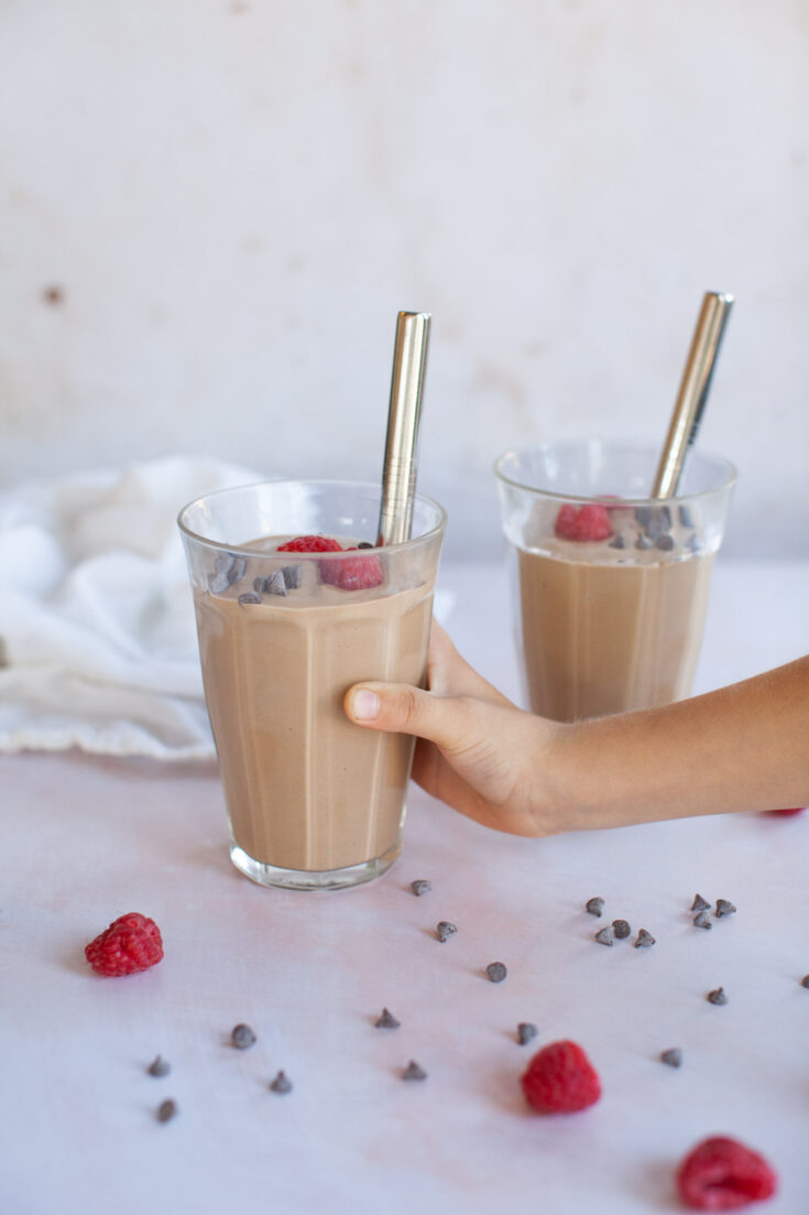 a hand reaches for a glass containing a smoothie.