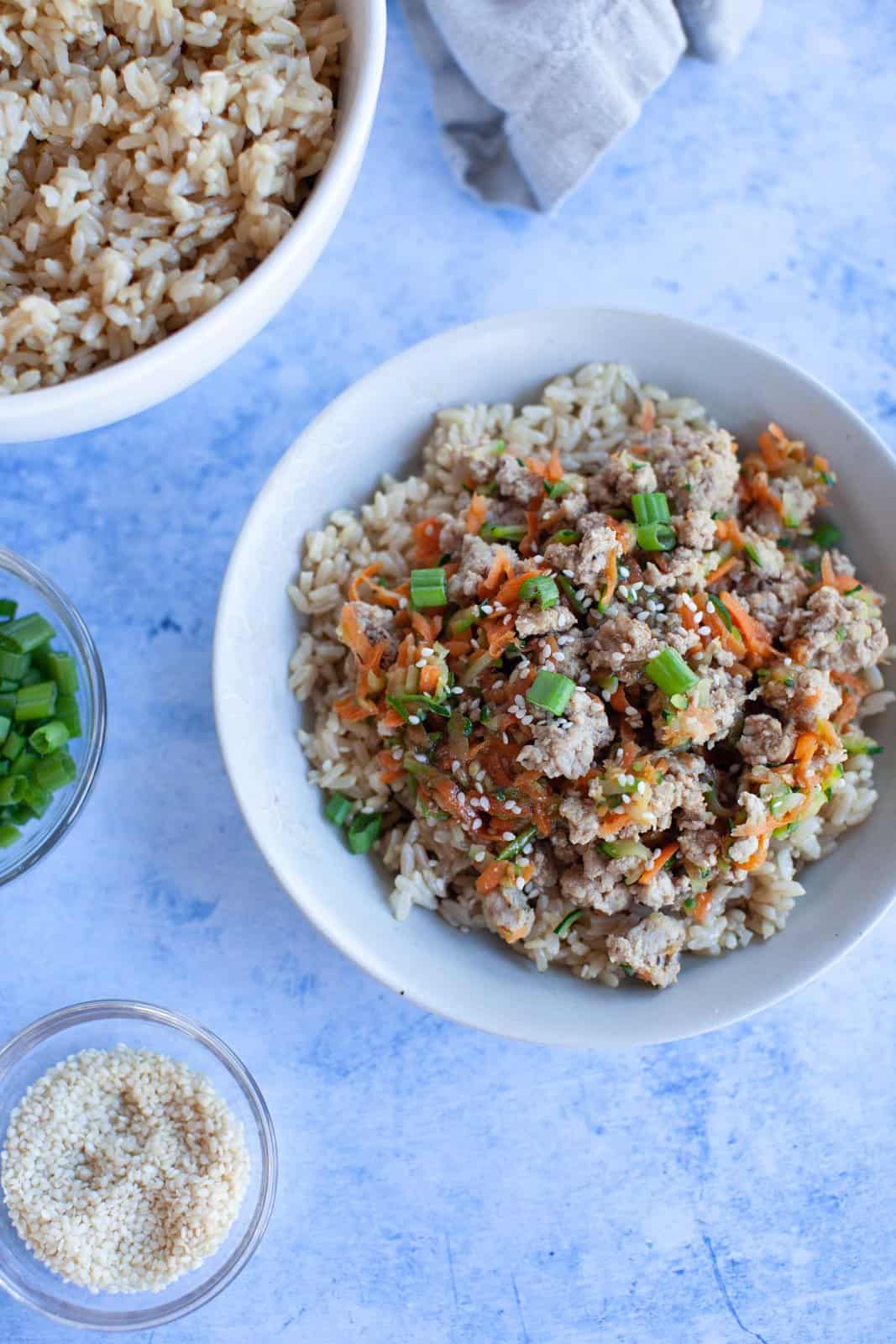a white bowl of brown rice topped with turkey stir fry