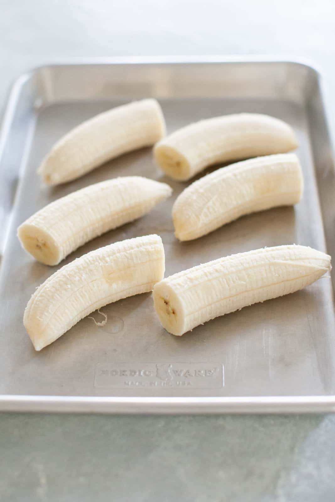 Three halved bananas on a baking sheet, ready for freezing.