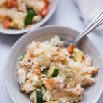 Gray dish filled with creamy chicken risotto with zucchini and tomatoes. With forks stuck into food.