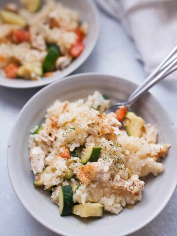 Gray dish filled with creamy chicken risotto with zucchini and tomatoes. With forks stuck into food.