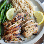 chicken thighs cut into slices on a plate garnished with lemons and green beans and rice.
