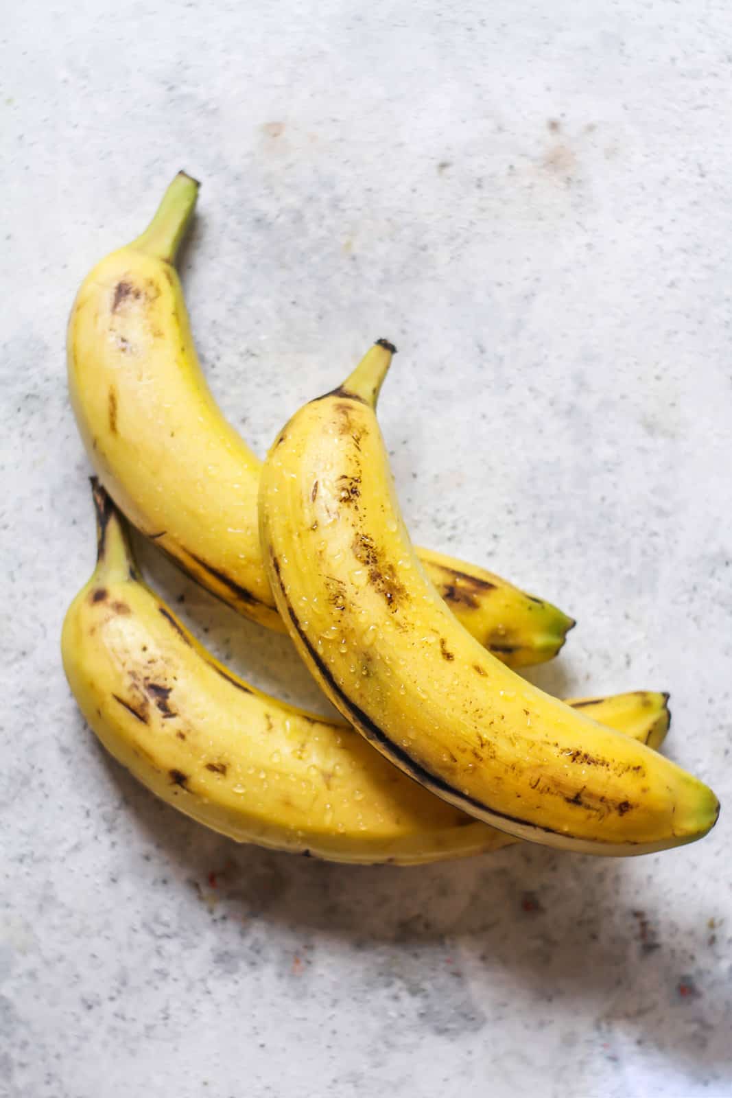 Three ripe, unpeeled bananas on a gray background.