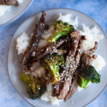 Beef and broccoli stir fry on a plate that is on a blue countertop