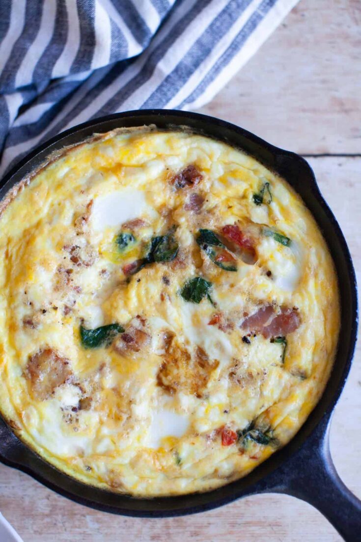 Overhead picture of the frittata in a cast-iron skillet with a blue and white stripped cloth in the upper-left corner.