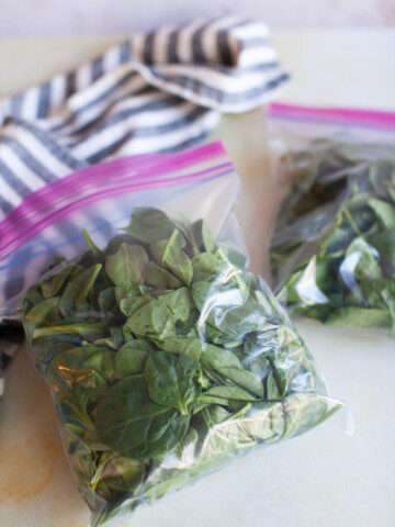 Two closed Ziploc bags of spinach on the counter.