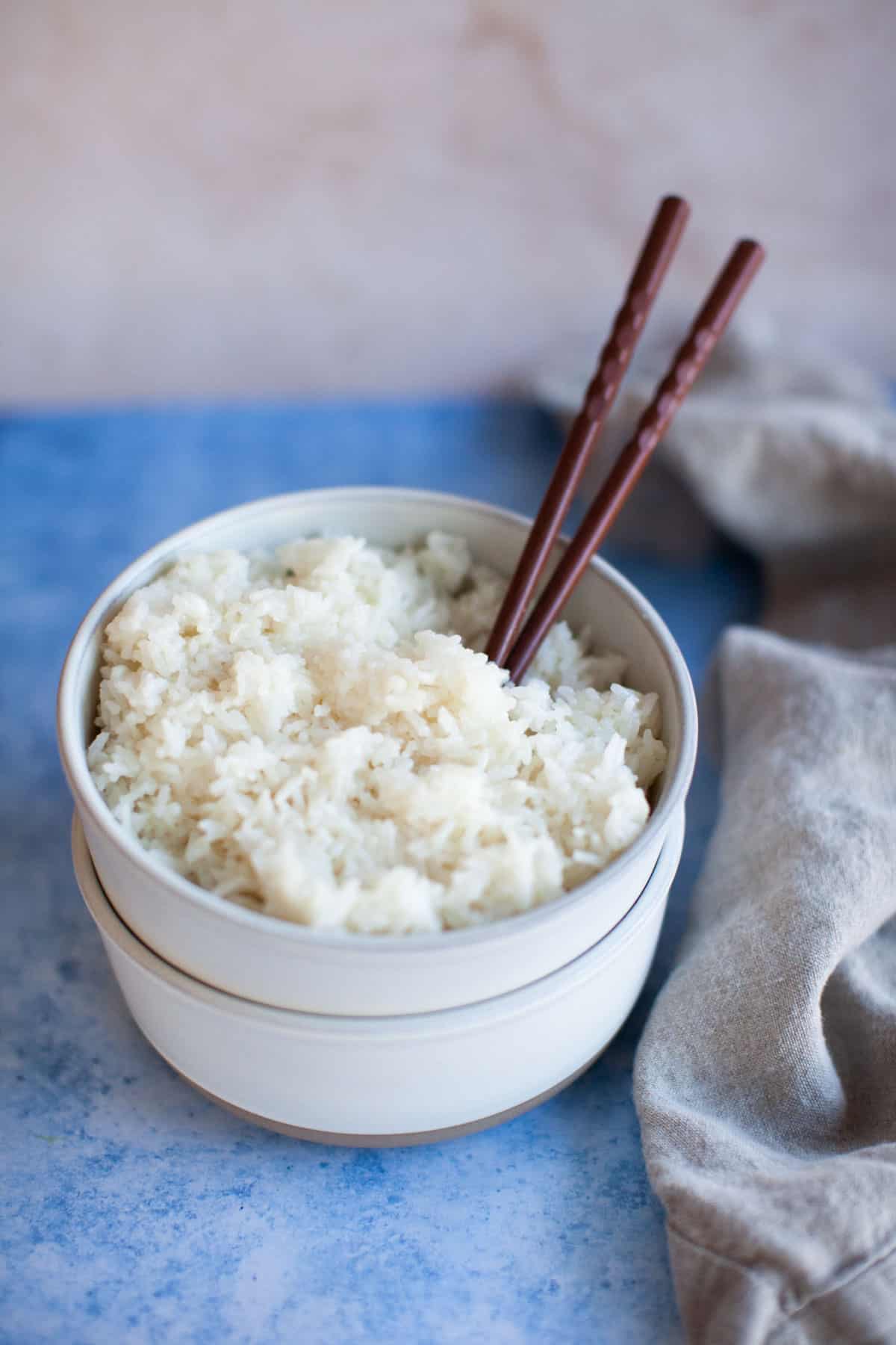 A close-up shot of jasmine rice in a white bowl, stacked on an empty bowl.