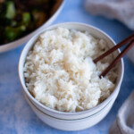 Overhead shot of plain white jasmine rice in a white bowl on a blue countertop.