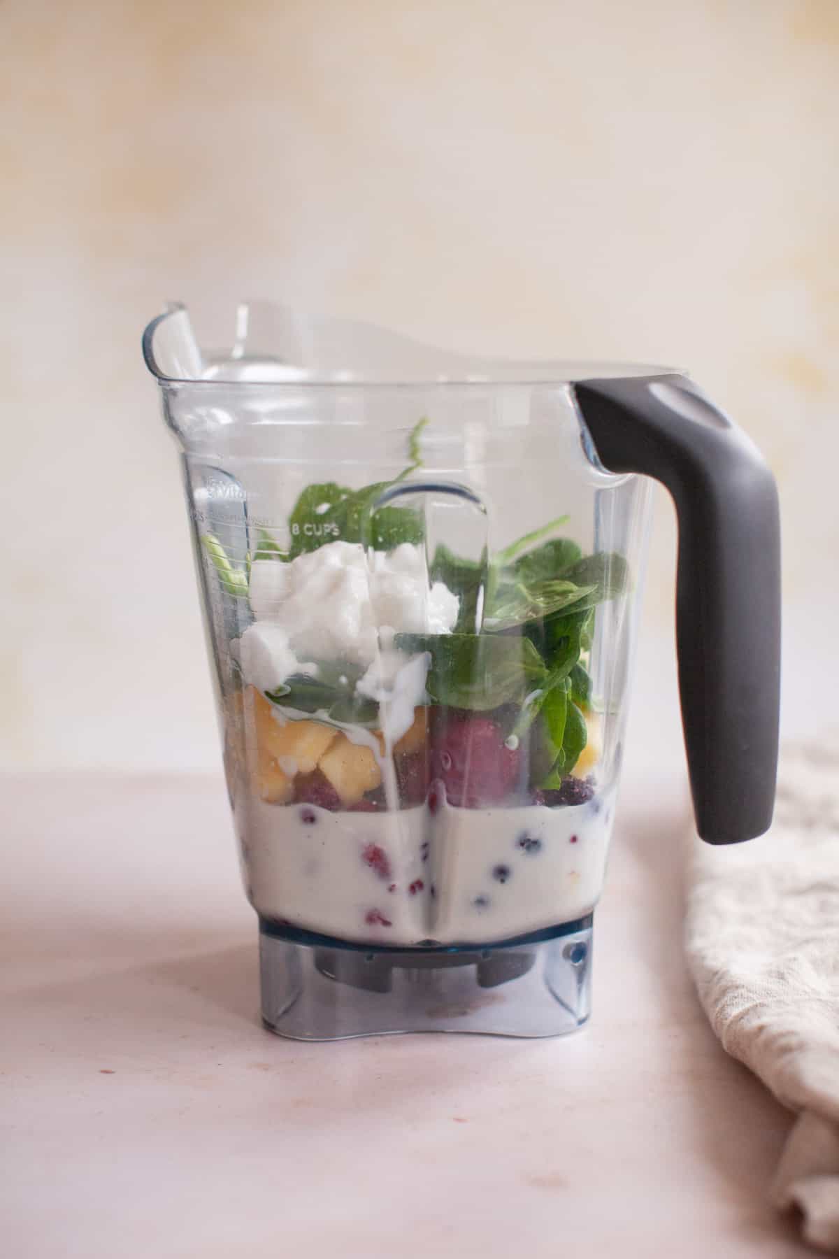 Mixed berries, spinach, yogurt, and almond milk unblended in the blender.