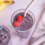 Overhead photo of one smoothie-filled glass with a straw, topped with fresh raspberries.