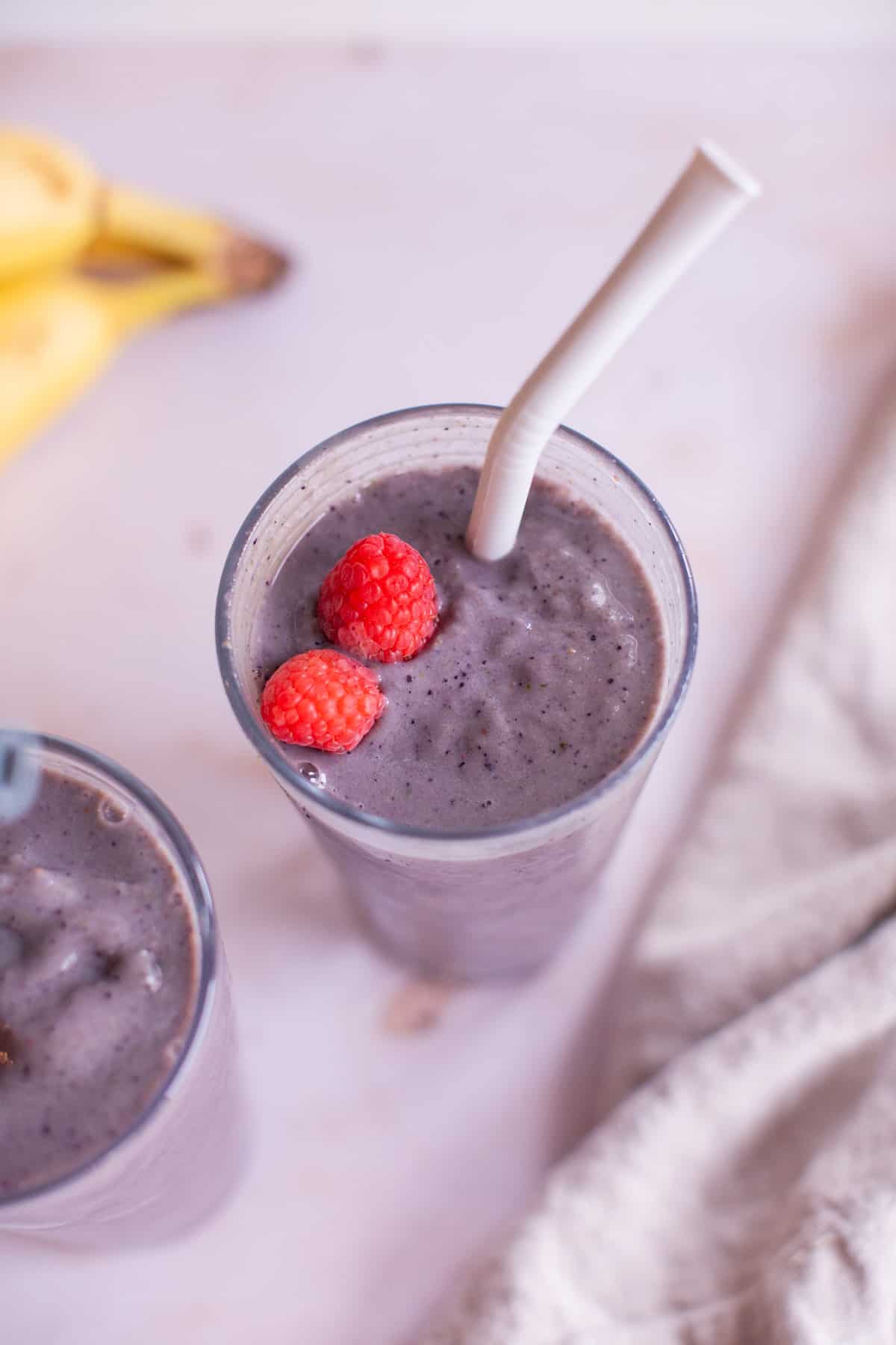 Overhead photo of one smoothie-filled glass with a straw, topped with fresh raspberries.